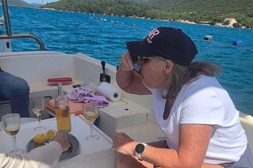 A person on a boat with a table set with drinks and a bottle, surrounded by water and distant land. 3