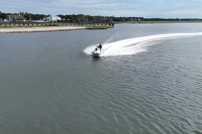 A person jet-skiing on a calm body of water with a bridge and buildings in the background. 2