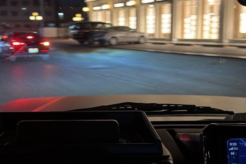 A nighttime city street from inside a car with a dashboard and a digital clock displaying 9:20. 2