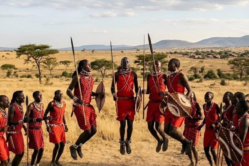 A group of people in red traditional attire, some holding spears, in a savannah landscape with sparse trees and distant mountains. 2