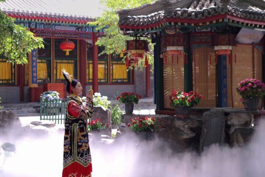 A person in traditional attire standing in a courtyard with a building featuring a tiled roof and red decorations. 5