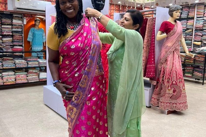 A clothing store with racks of colorful saris and a mannequin dressed in a pink and red sari. 4
