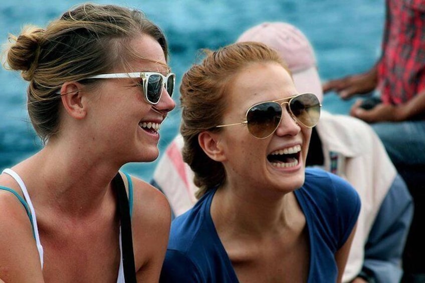 Two people wearing sunglasses, one in a blue top and the other in a white top, with a body of water in the background. 1