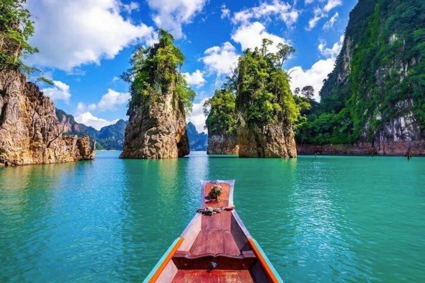 A wooden boat on clear turquoise water with rocky formations and lush greenery on the sides. 3