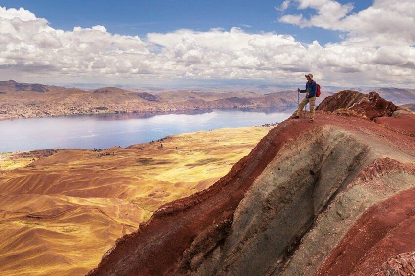 A hiker on a red-brown terrain with a lake in the background. 2