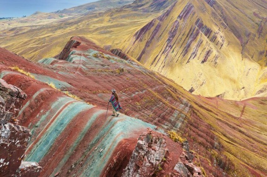A person hiking on a colorful mountain ridge with distinct red, yellow, and green layers. 4