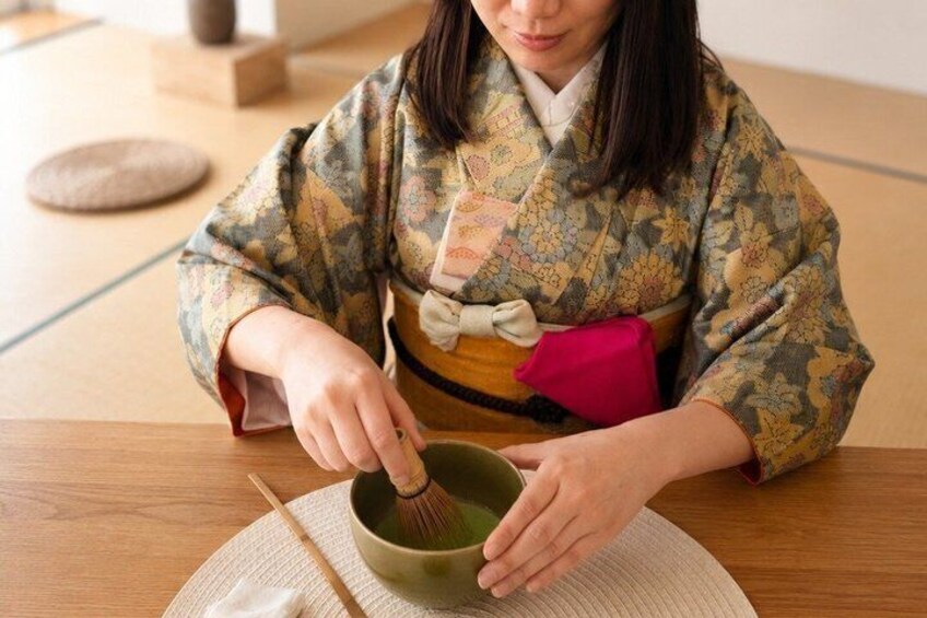 A person in traditional attire whisking a green liquid in a bowl. 5