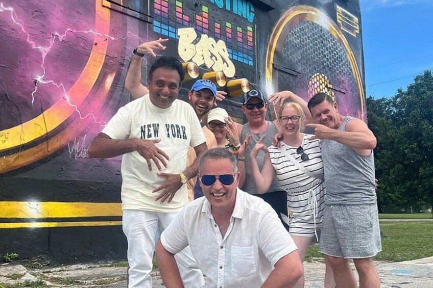 A group of people posing in front of a colorful mural with graffiti and lightning effects. 4