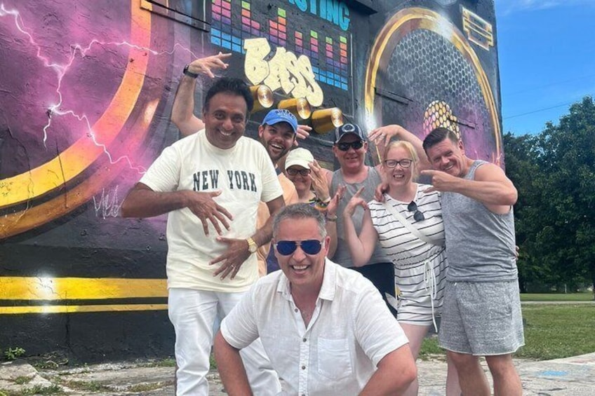 A group of people posing in front of a colorful mural with a guitar and lightning effects. 5