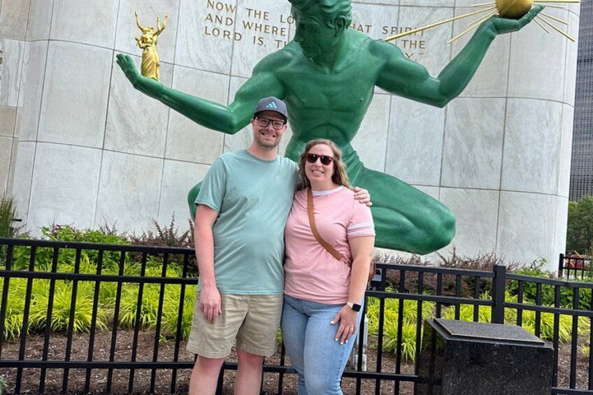 A man and a woman standing in front of a large green statue with a golden figure on a wall. 2