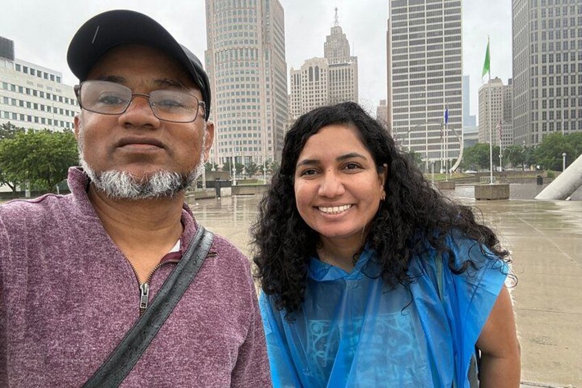 Two people standing in an urban setting with tall buildings and a flag in the background. 4