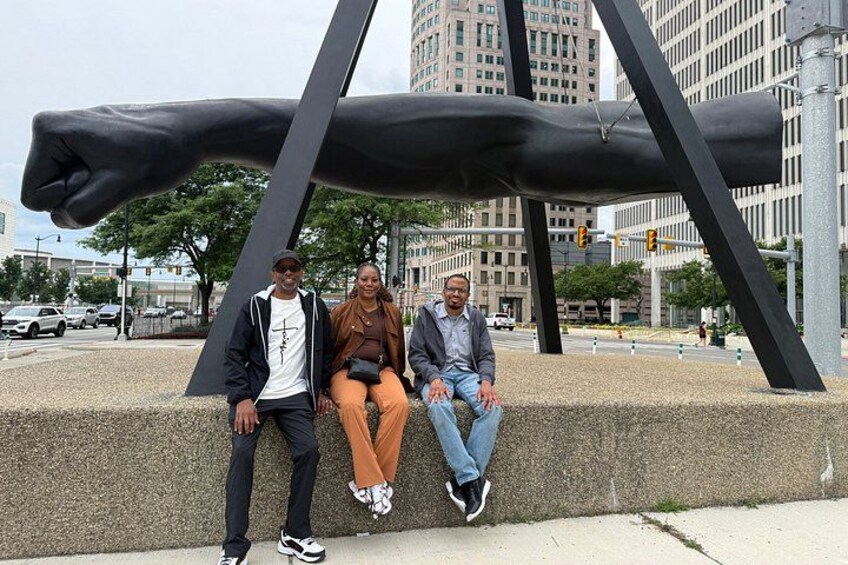 Three people sitting on a bench with a large abstract sculpture in the background. 3