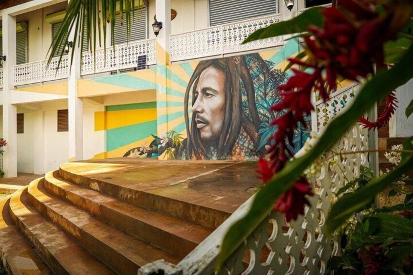 A mural on a building, a set of wooden stairs, and a white fence with red flowers. 1