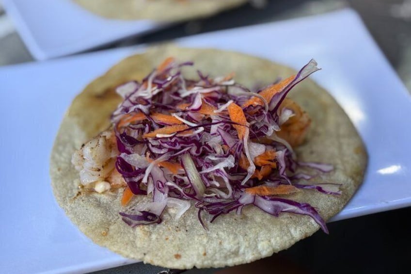 A taco with shredded purple and orange vegetables on a white plate. 3