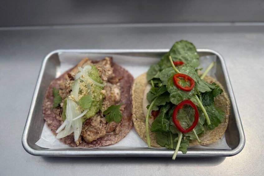 Two tacos on a metal tray, one with meat and the other with lettuce and red chili slices. 4