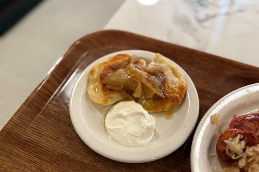 A plate with a stuffed pastry and a dollop of sour cream on a wooden tray. 2