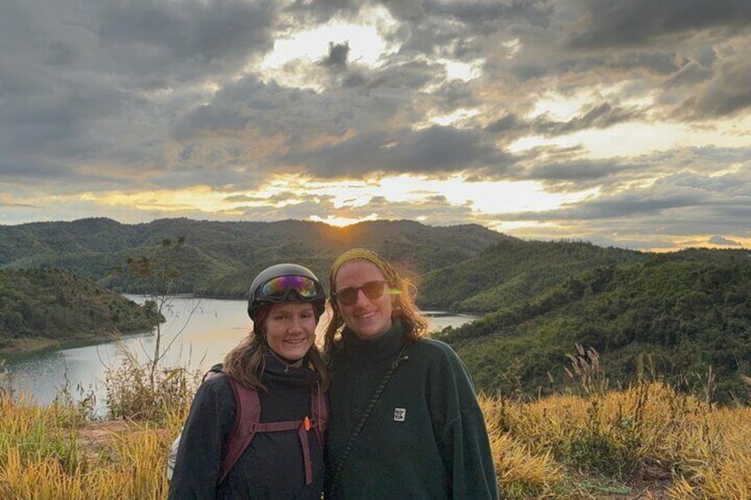Two people standing on a hill overlooking a lake with a sunset in the background. 2
