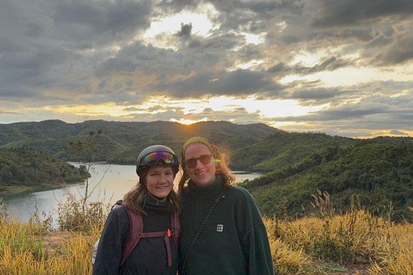 Two people standing on a hill overlooking a lake with a sunset in the background. 2