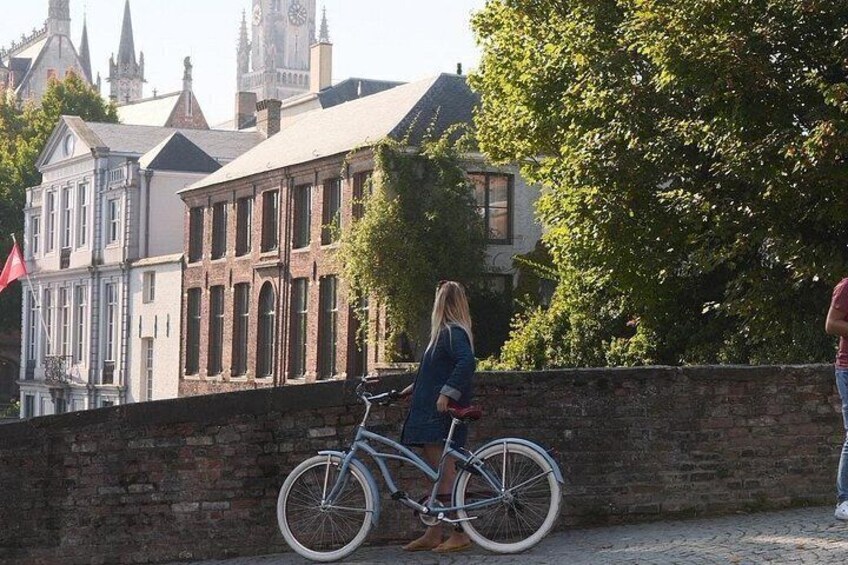 A person standing next to a bicycle on a cobblestone path, with historic buildings and a flag in the background. 4