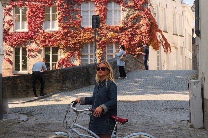 A person standing next to a bicycle on a cobblestone street with buildings in the background. 1