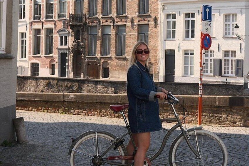 A woman standing next to a bicycle on a cobblestone street with historic buildings in the background. 3