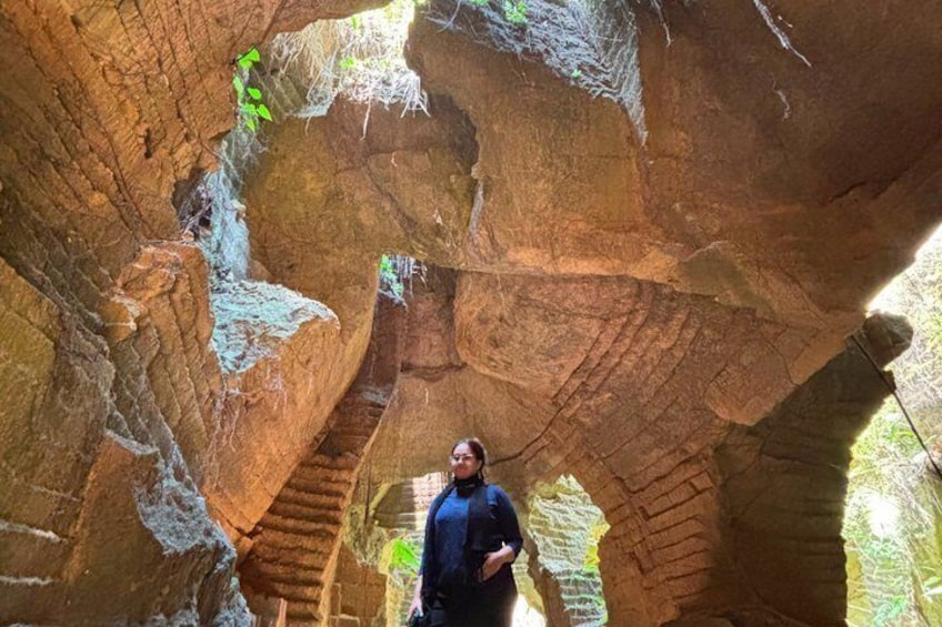 A person standing in a rock formation with a natural archway. 1