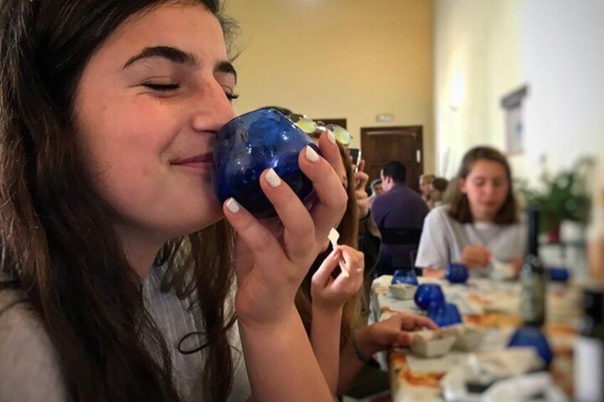 A person holding a blue object, possibly a cup, in a room with other people seated at tables. 5