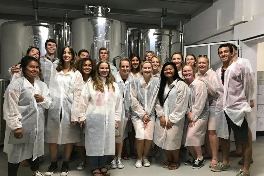 A group of people in a laboratory setting with stainless steel tanks and a whiteboard in the background. 2