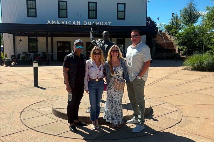 A group of people standing in front of a building labeled 'AMERICAN OUTPOST.' 5