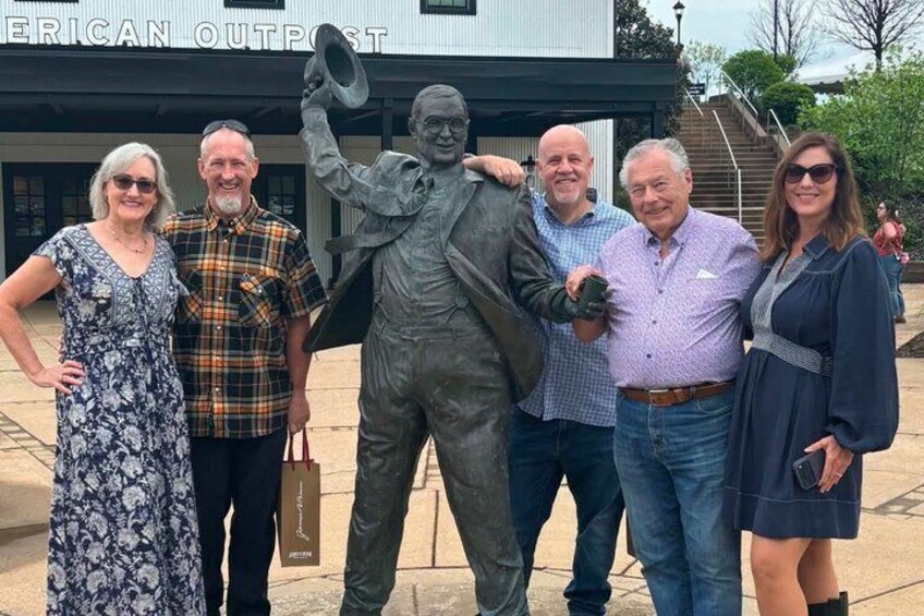 A group of people posing with a statue in front of a building labeled 'AMERICAN OUTPOST.' 3