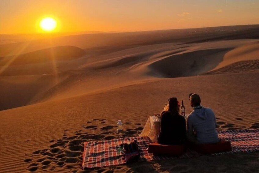 Two people sitting on a blanket in a desert at sunset. 3