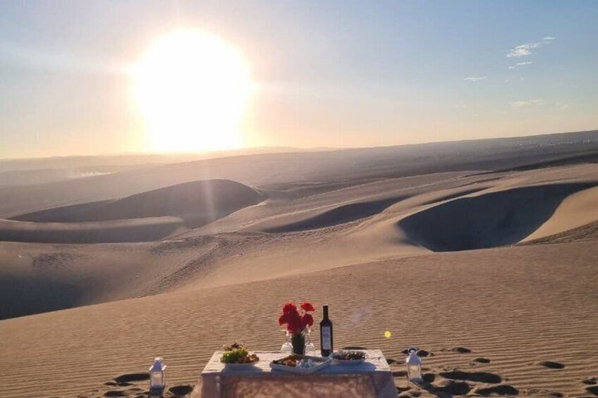 A desert landscape with sand dunes and a table with a bottle and flowers. 2