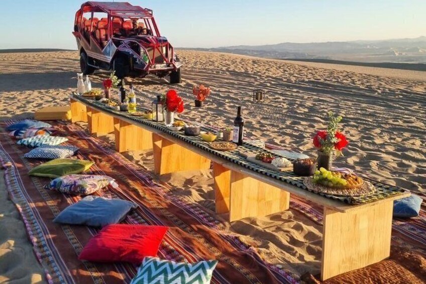 A desert scene with a wooden table set up on the sand, a red vehicle in the background, and a clear sky. 5