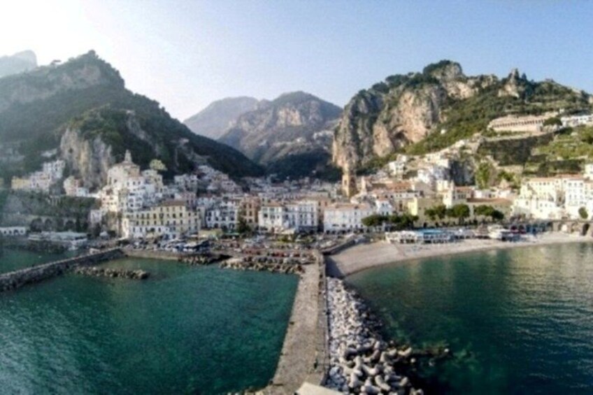A coastal town with buildings along the waterfront, a rocky peninsula, and mountains in the background. 3