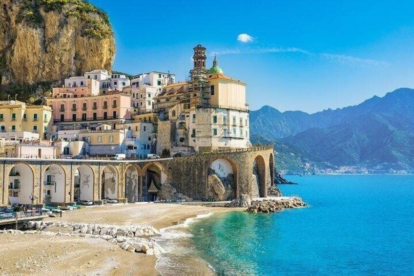 A coastal town with a prominent church, a stone bridge, and a mountain backdrop. 1