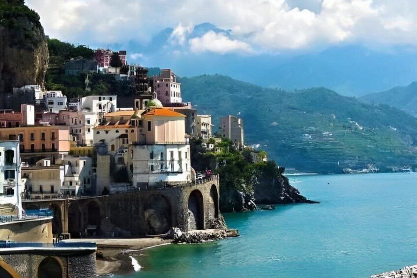 A coastal town with buildings on a cliff, a bridge, and a calm sea. 2
