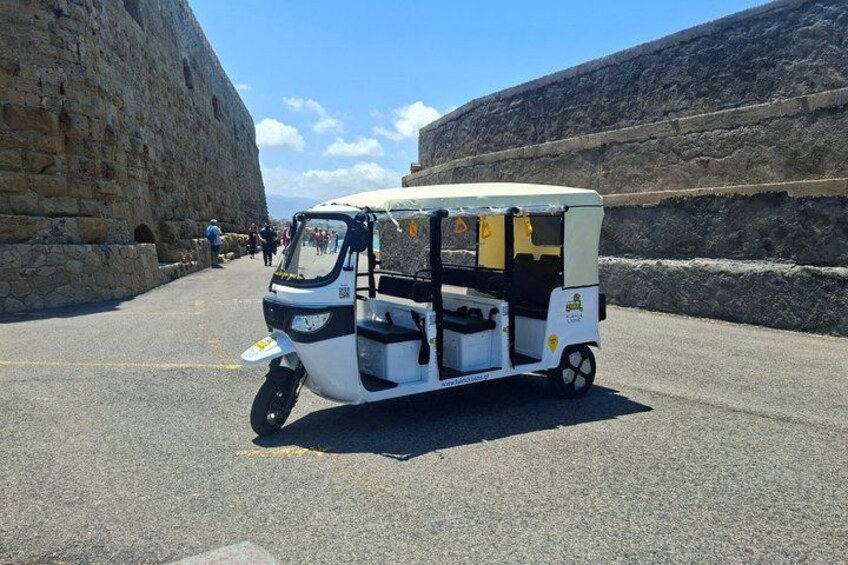 A white three-wheeled vehicle parked on a paved road with stone walls on either side. 4