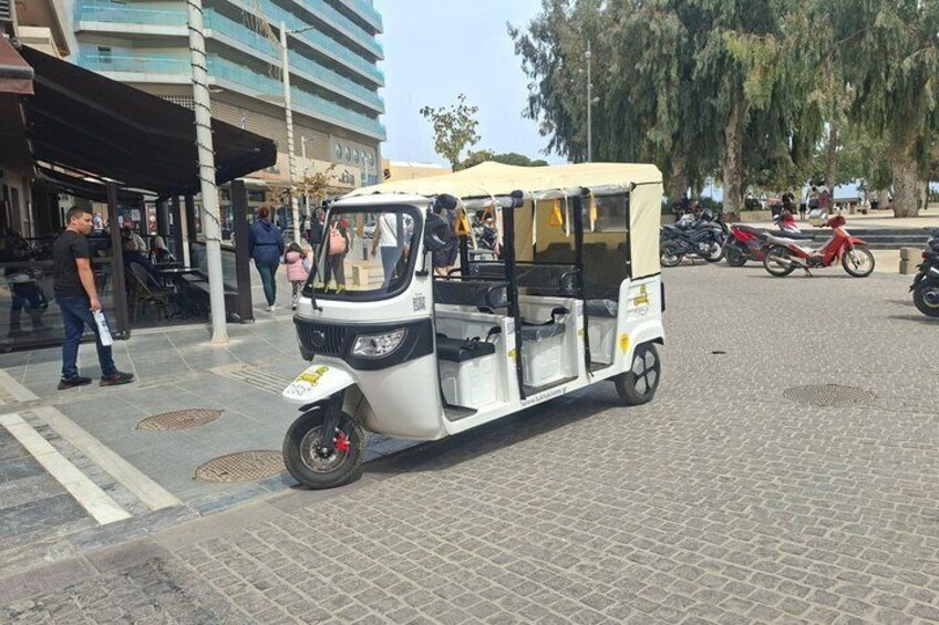 A tuk-tuk parked on a cobblestone street with pedestrians and a building in the background. 3