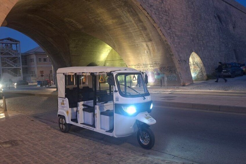 A tuk-tuk parked under a large stone bridge at night. 5
