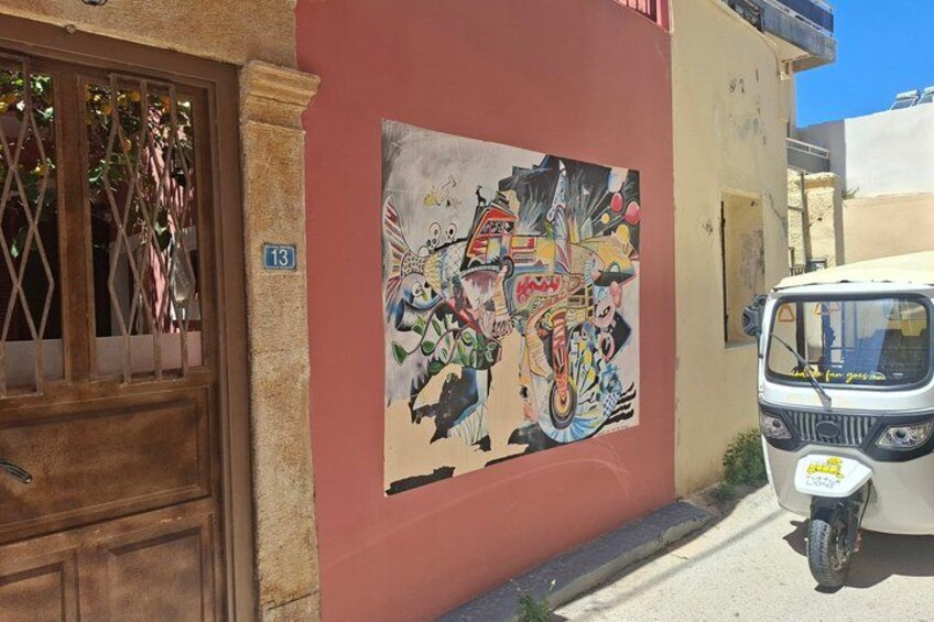 A building with a colorful mural, a wooden door, and a parked tuk-tuk. 2