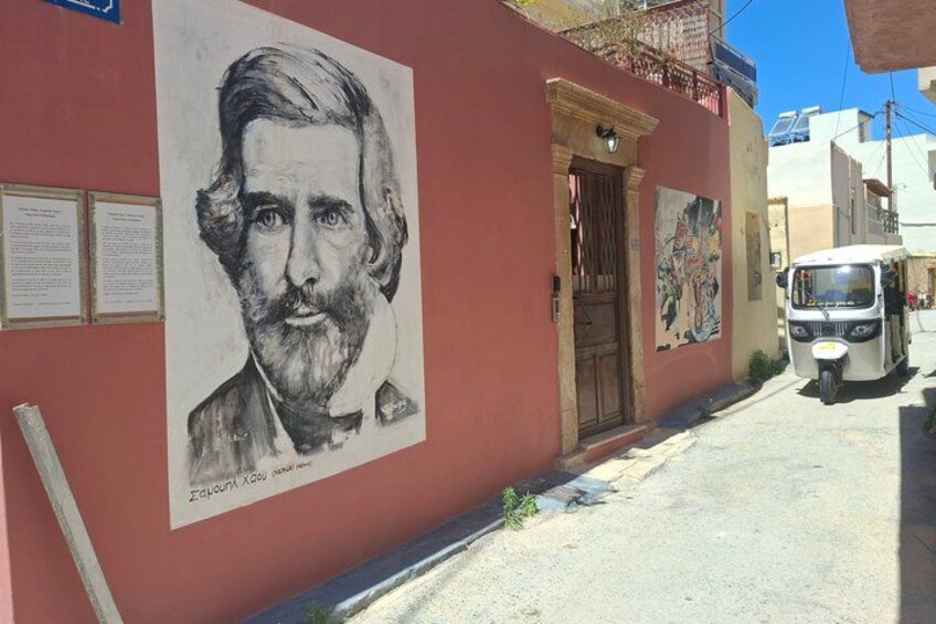 A street with a red building, a portrait mural, and a parked tuk-tuk. 3