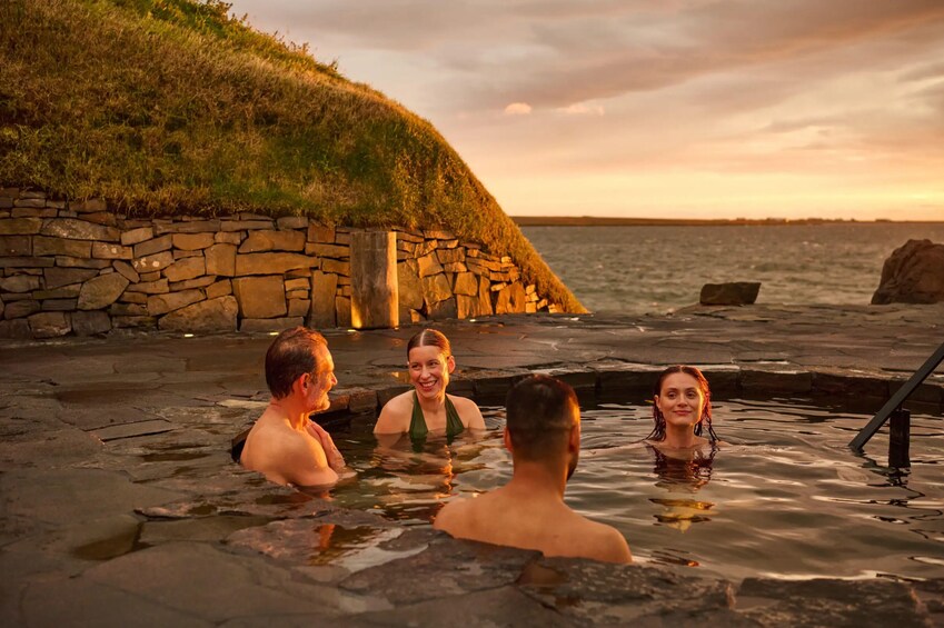 En gruppe mennesker i et stenhusbad område ved havet i solnedgangen. 3