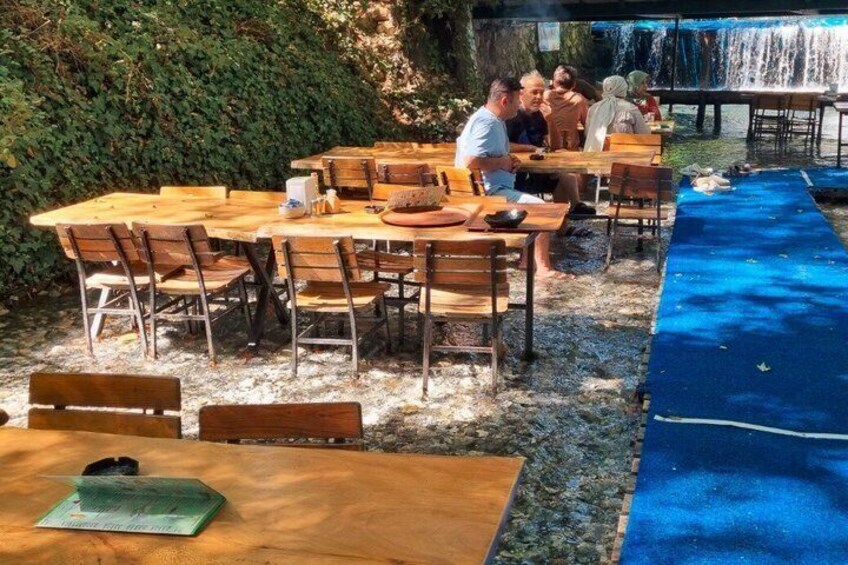 Outdoor wooden tables and chairs, a blue mat, and a waterfall in the background. 2