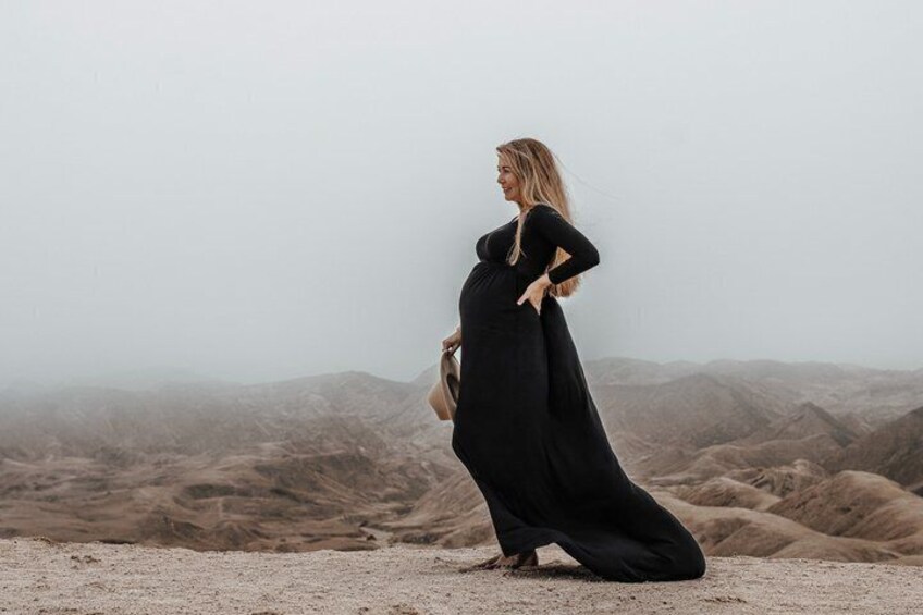 A person in a long black dress standing on a barren landscape with mountains in the background. 2