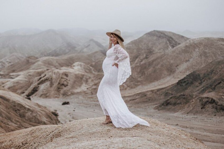 A person in a white dress standing on a rocky outcrop with a mountainous landscape in the background. 1