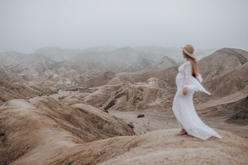 A person in a white dress standing on a rocky terrain with a mountainous backdrop. 5