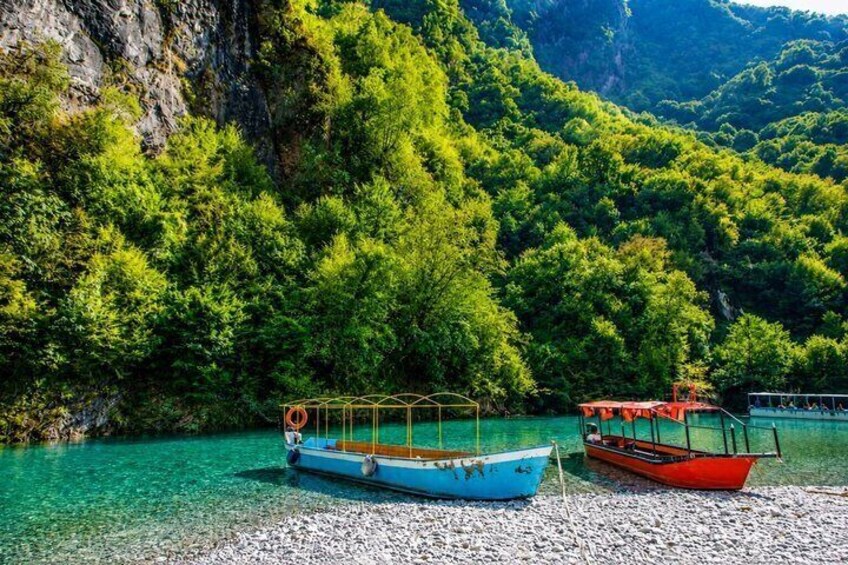 Two boats on a pebbly shore with a forested mountain backdrop. 2