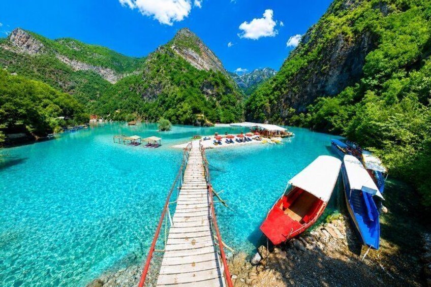 A wooden pier leading to a turquoise lake surrounded by lush green mountains. 1