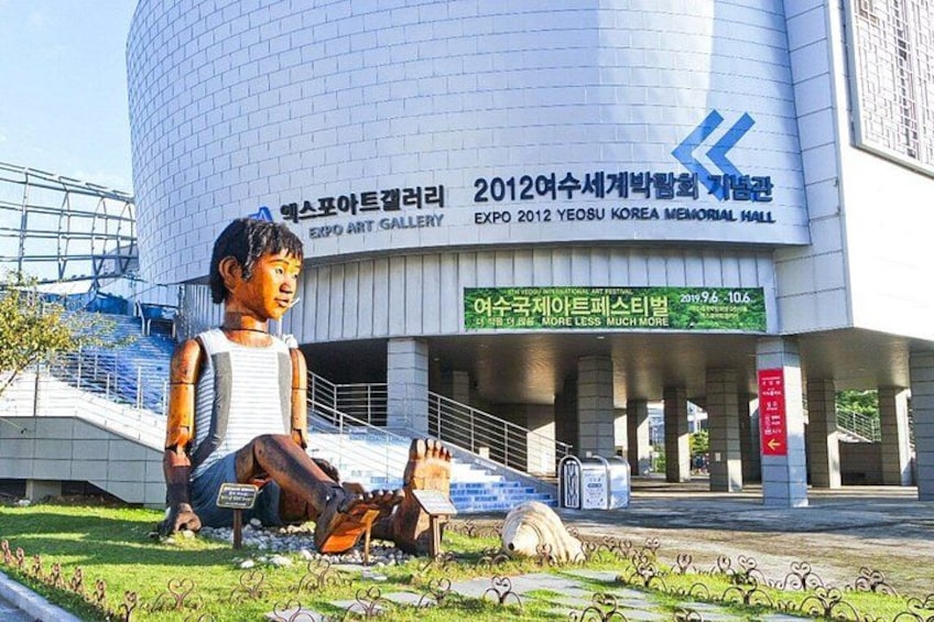 A large sculpture of a child in front of a building with a sign reading 'EXPO 2012 Yeosu Korea Memorial Hall'. 5