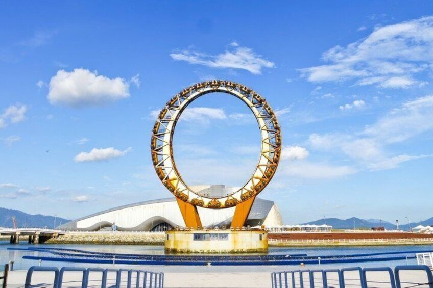 A Ferris wheel with a circular structure, a large white building in the background, and a clear blue sky. 3